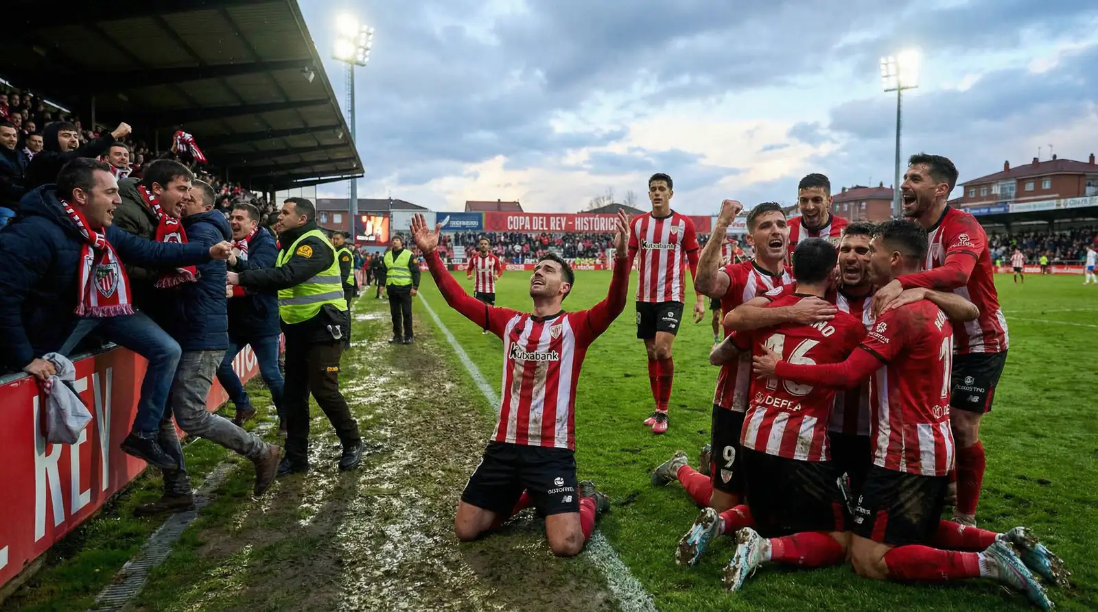 Jugadores de equipo modesto celebrando apasionadamente una victoria historica de Copa del Rey ante sus aficionados emocionados